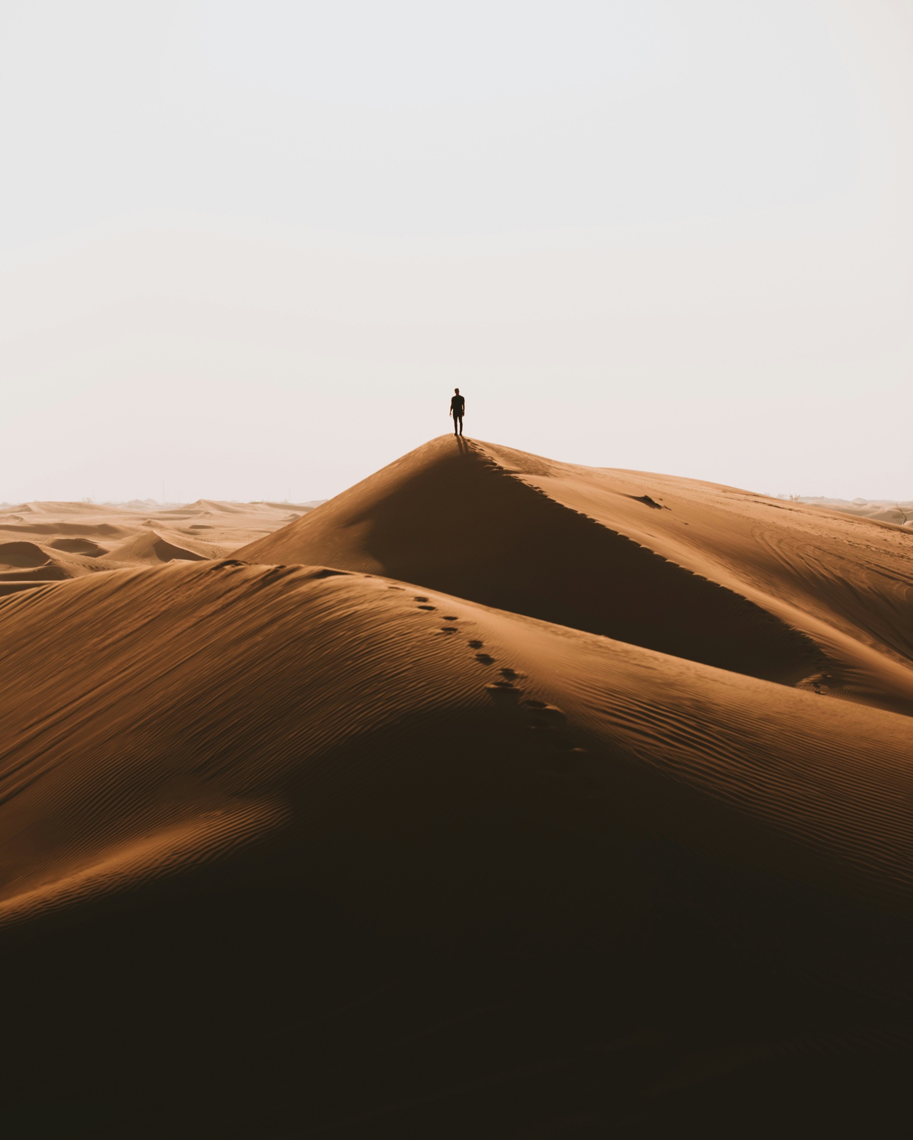 A lone figure walking the crest of a desert dune at dusk.